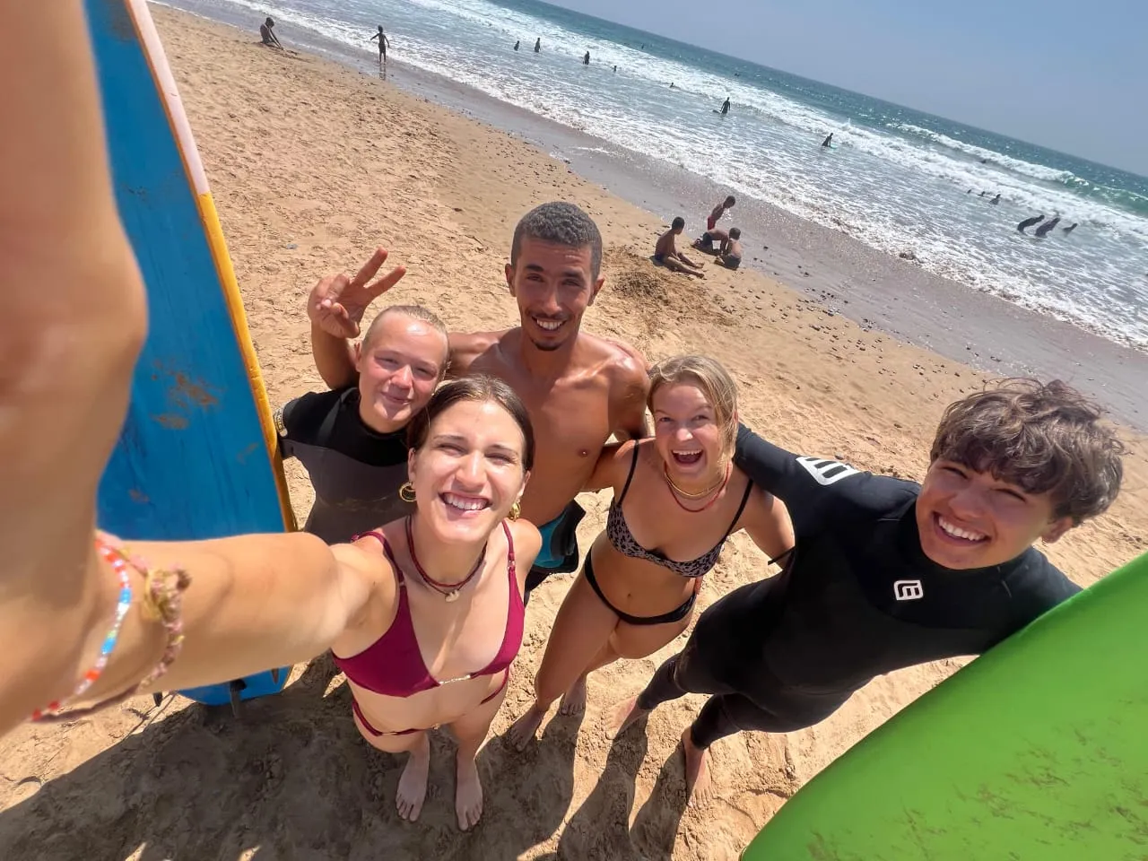 Group of four young surfers laughing with coach Simo after a group surf session on the Agadir coast