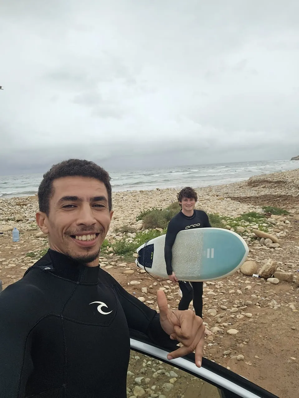 Coach Simo and an intermediate student smiling beside a car after an early-morning surf session at a remote Agadir break