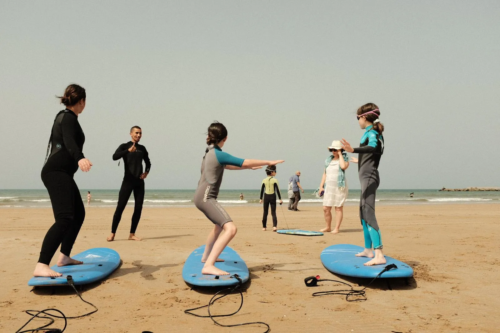 Coach Simo teaching three students the pop-up stance on the sand before a surf session at Agadir Beach