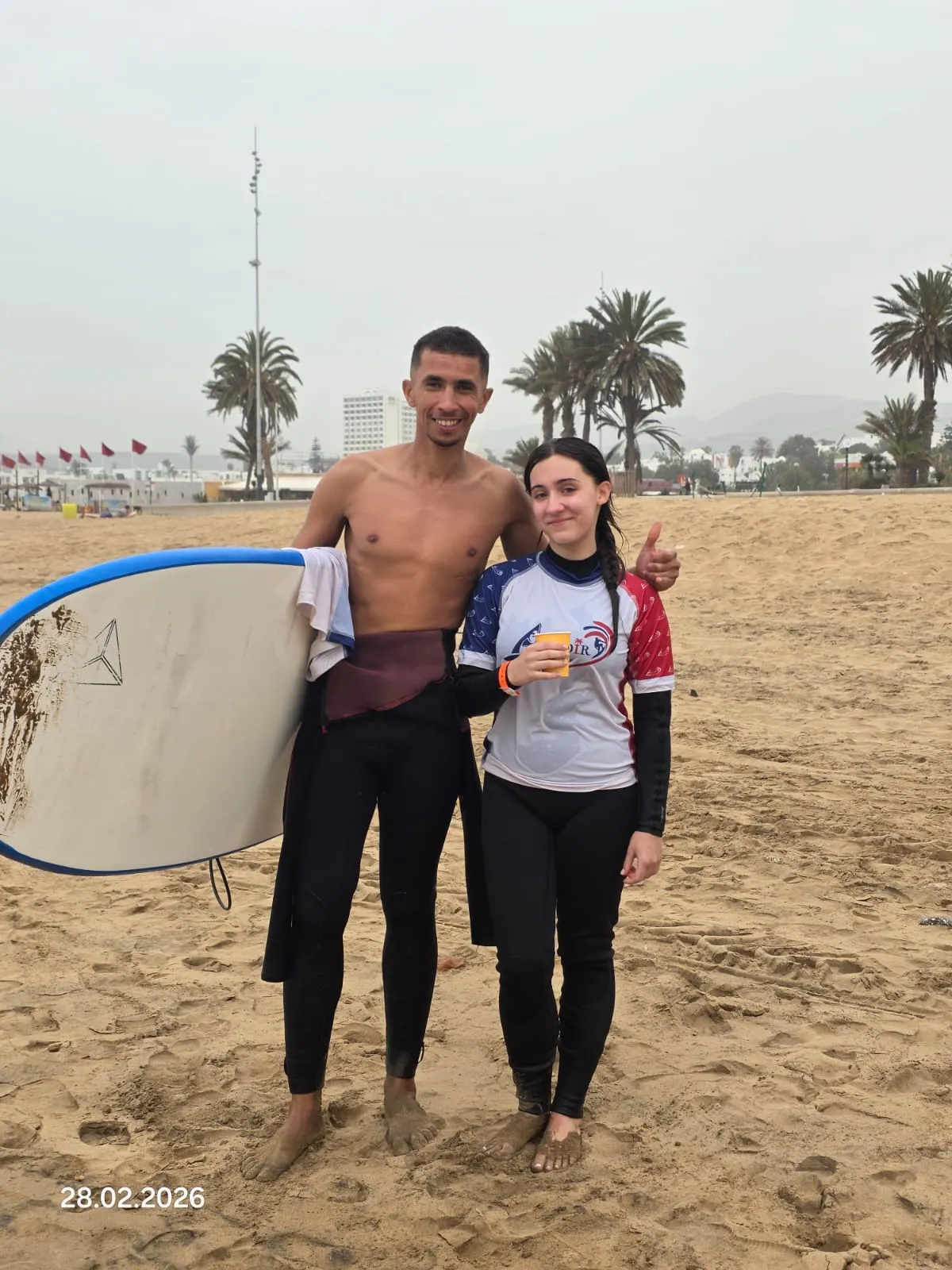 Coach Simo and a solo surf student smiling on the beach with palm trees and red flags behind, after a one-on-one session