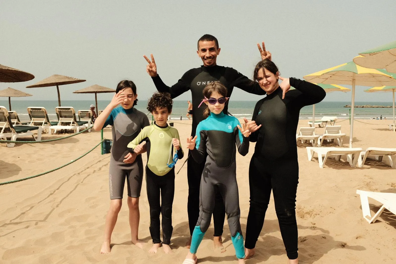 Coach Simo with four kids in wetsuits posing on the sand after a family surf session in Agadir
