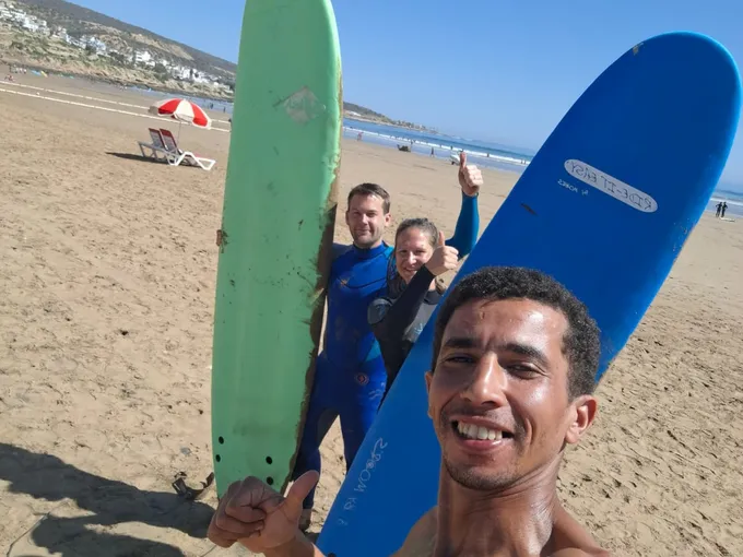Two friends posing with surfboards and coach Simo after a coached session in Agadir