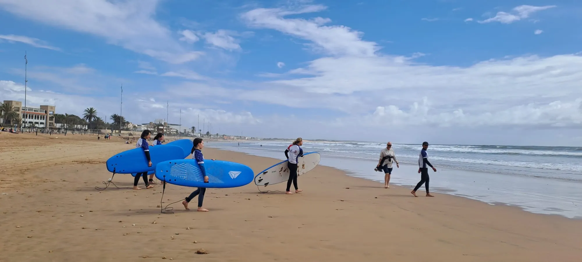 Five surf students walking down the beach with foam boards toward the Atlantic at Agadir Beach